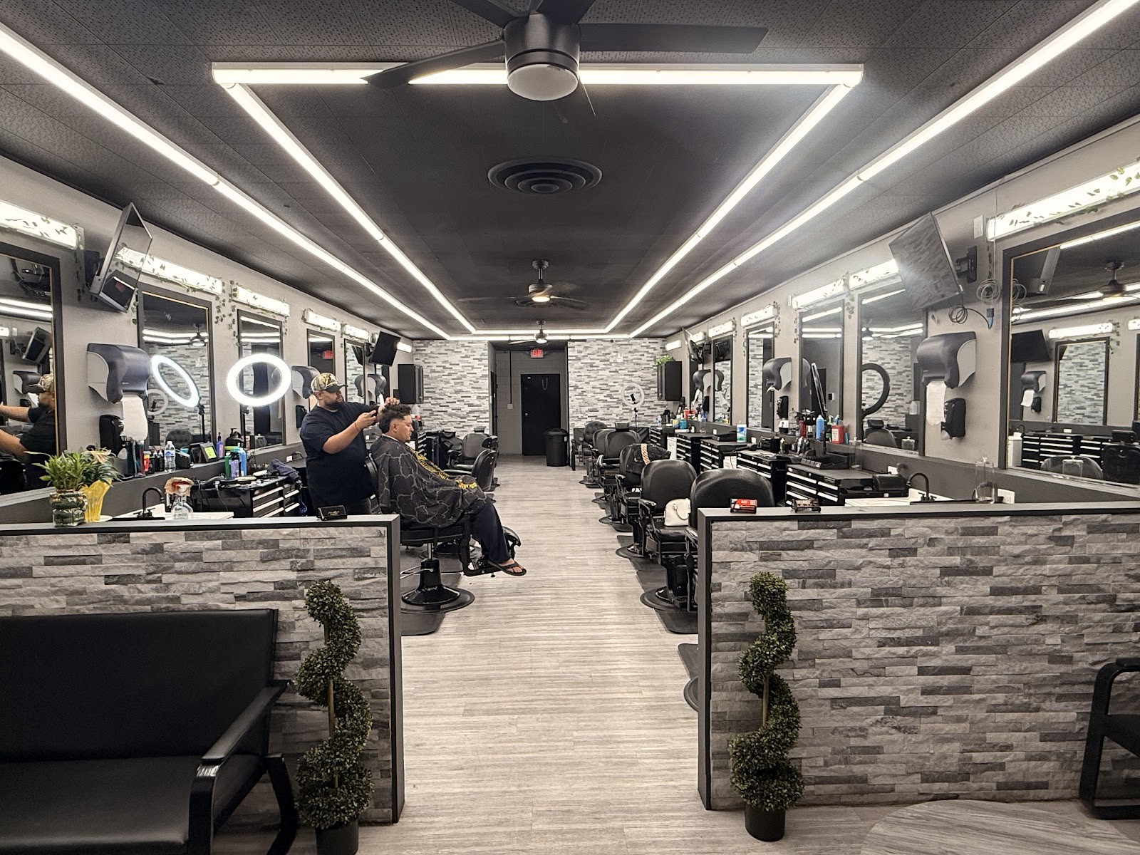 Interior of barbershop with barber cutting a client's hair and rows of stations